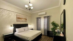 A bedroom with a bed, bedside tables, a chandelier, an air conditioning unit, a potted plant, and a mirror. - New Cairo Gem 3BR Villa w/ Garden, Near Shopping & Dining by Best of Bed'z (cairo)
