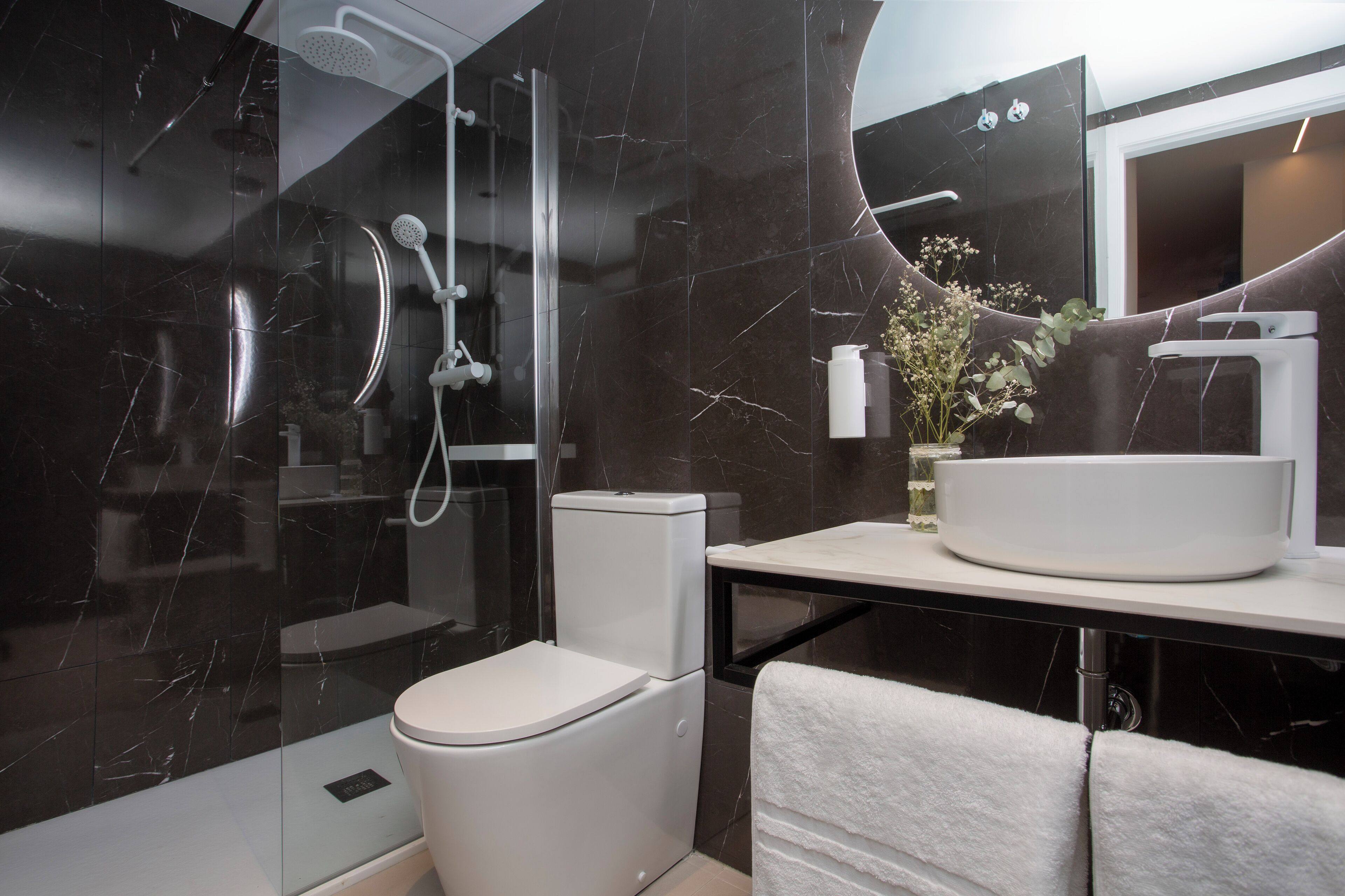 A modern bathroom with a glass-enclosed shower, a white toilet, a sink with a mirror, and a towel rack.