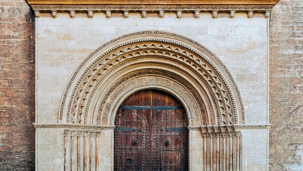 Un'ampia porta in legno decorata con elaborate sculture e un arco in pietra.