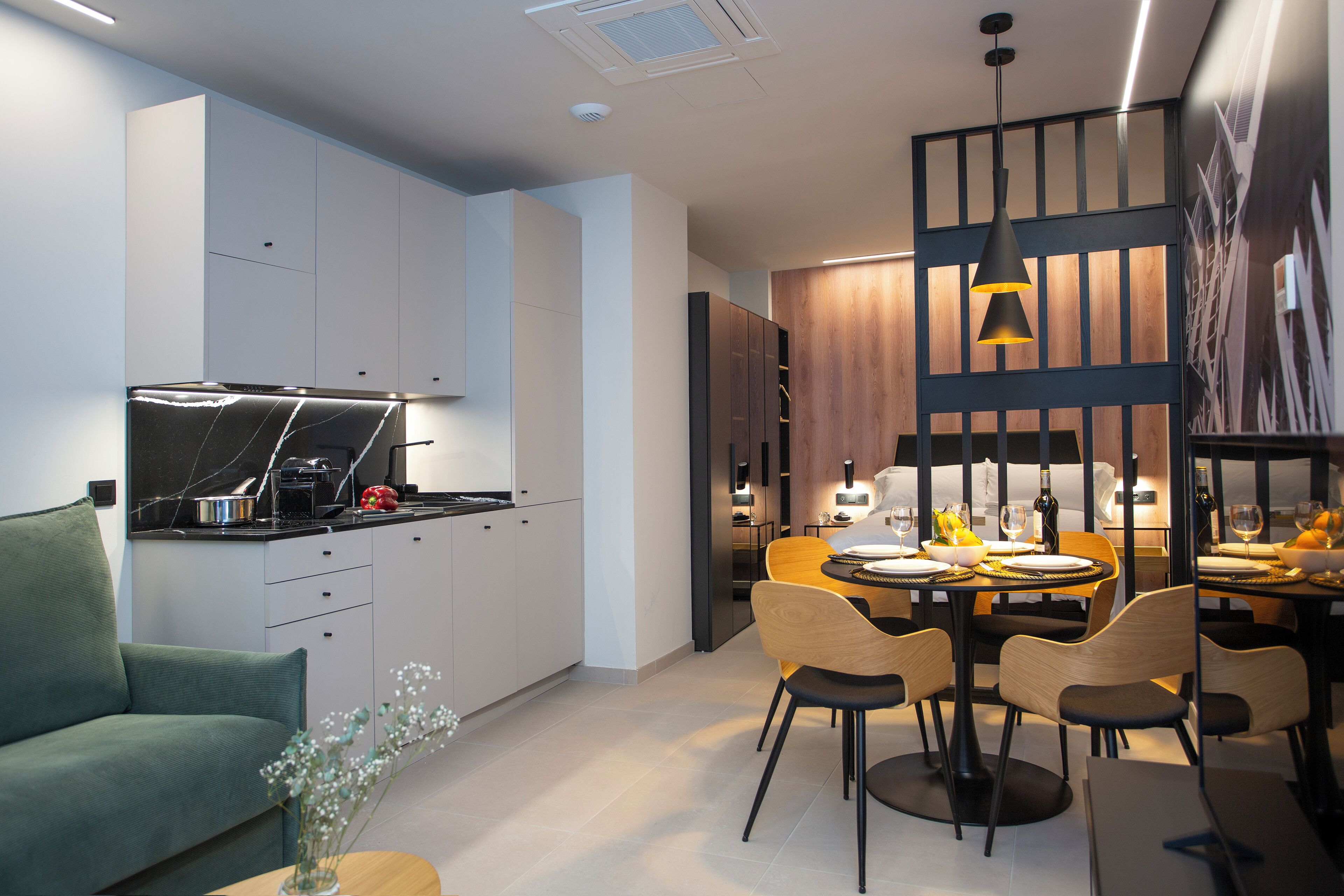 Una cocina moderna con estufa integrada, un comedor con mesa y sillas de madera, y una sala de estar con un sofá verde.