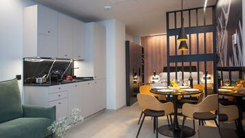 Una cocina moderna con estufa integrada, un comedor con mesa y sillas de madera, y una sala de estar con un sofá verde.
