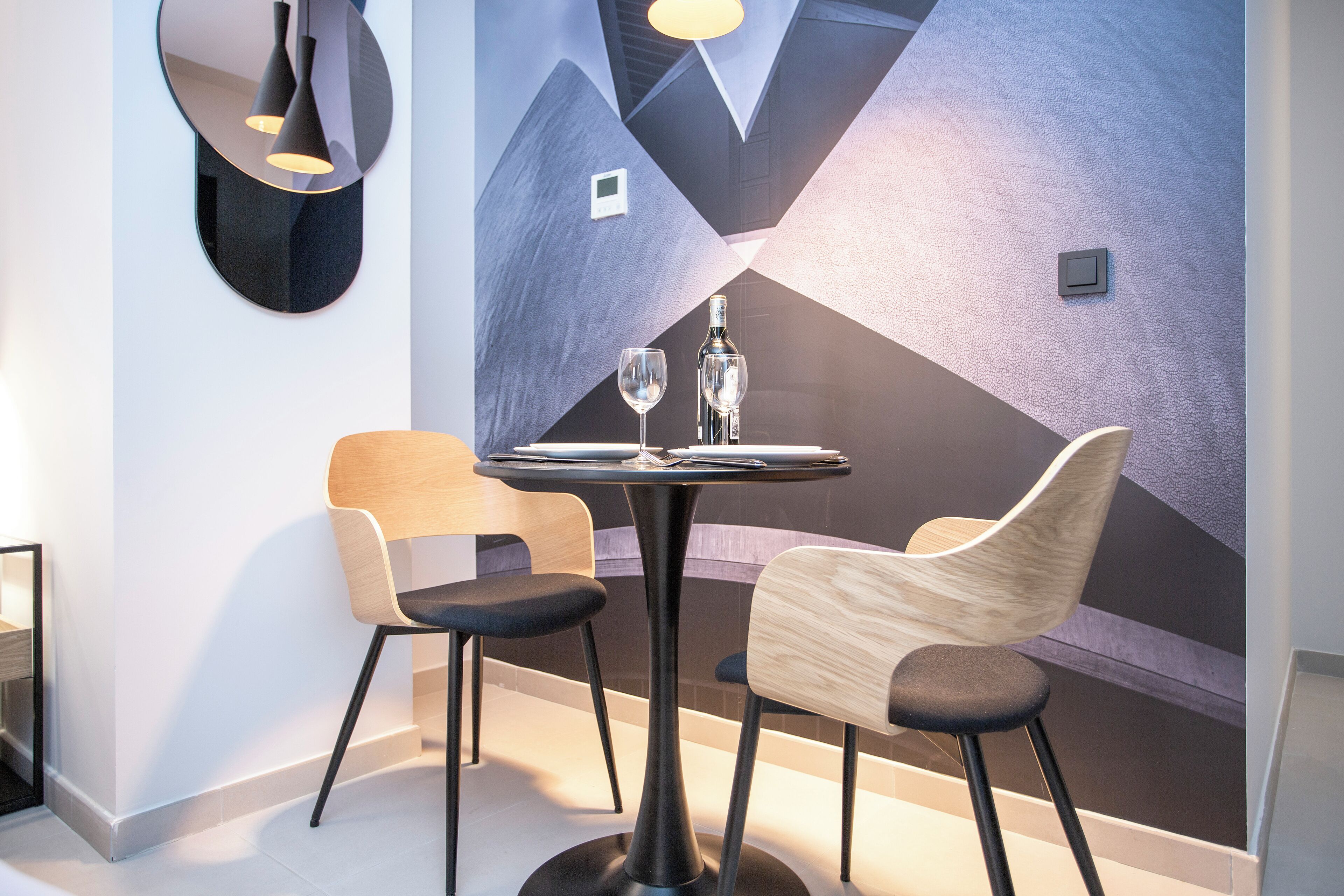 A modern dining area with a round table, two chairs, and a decorative wall.