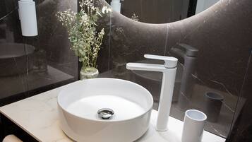Un baño moderno con un lavabo blanco redondo, un solo grifo y un pequeño jarrón con flores.