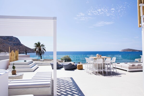 Een terras op het dak met witte meubels, een tafel en stoelen, met uitzicht op de kust, de zee en een berg in de verte.