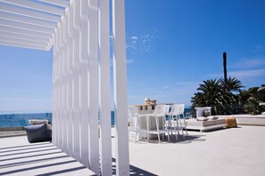 Een terras met witte meubels, een tafel met schalen en uitzicht op zee.