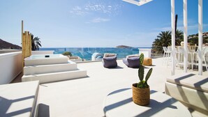 Une terrasse sur le toit, avec des meubles blancs, un cactus et une vue sur la mer.