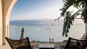 A balcony with two wicker chairs and a small table, overlooking a calm sea with birds flying. - Dali Nest Secret Garden Lake View Inn (Dali)