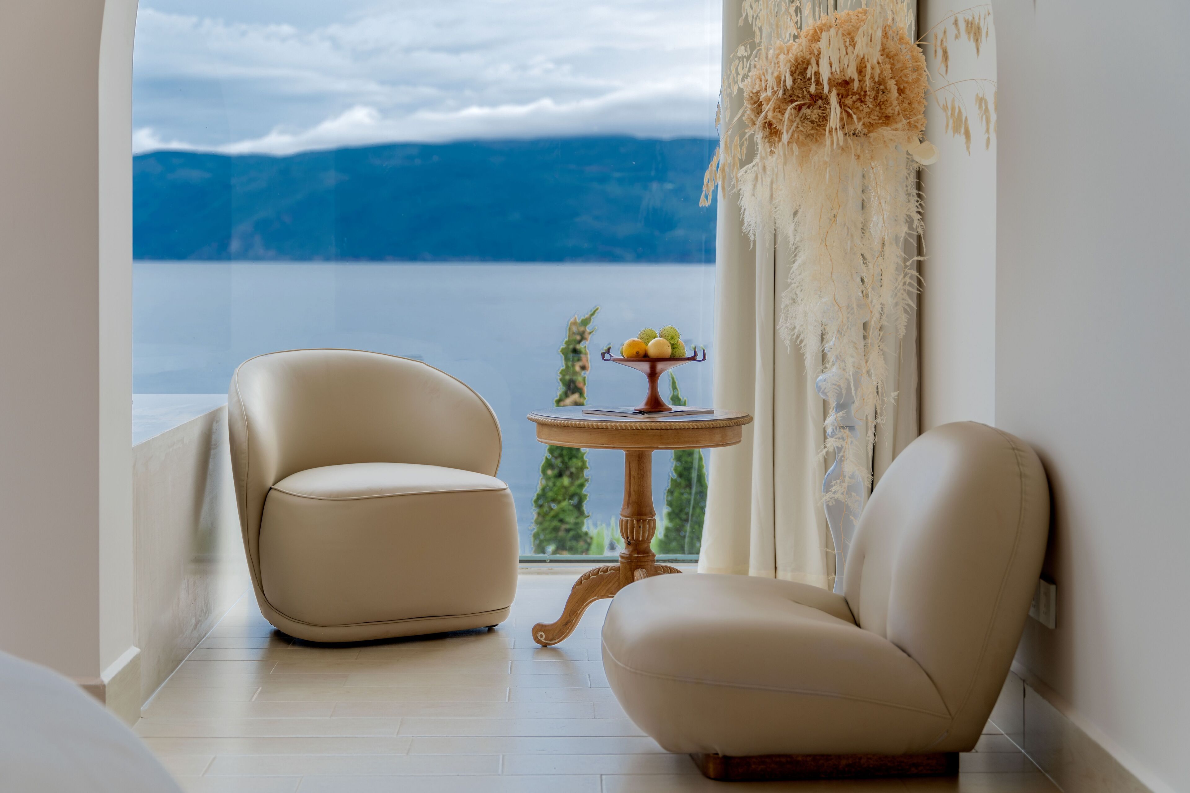 Une chambre avec vue sur un lac et des montagnes, comprenant deux fauteuils en cuir et une petite table sur laquelle sont disposés des fruits.