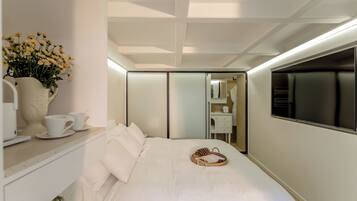 A modern hotel room with a neatly made bed, a bedside table with a vase of flowers, and a large mirror reflecting the room.