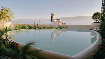 A woman sitting by a pool with a view of the sea and mountains.