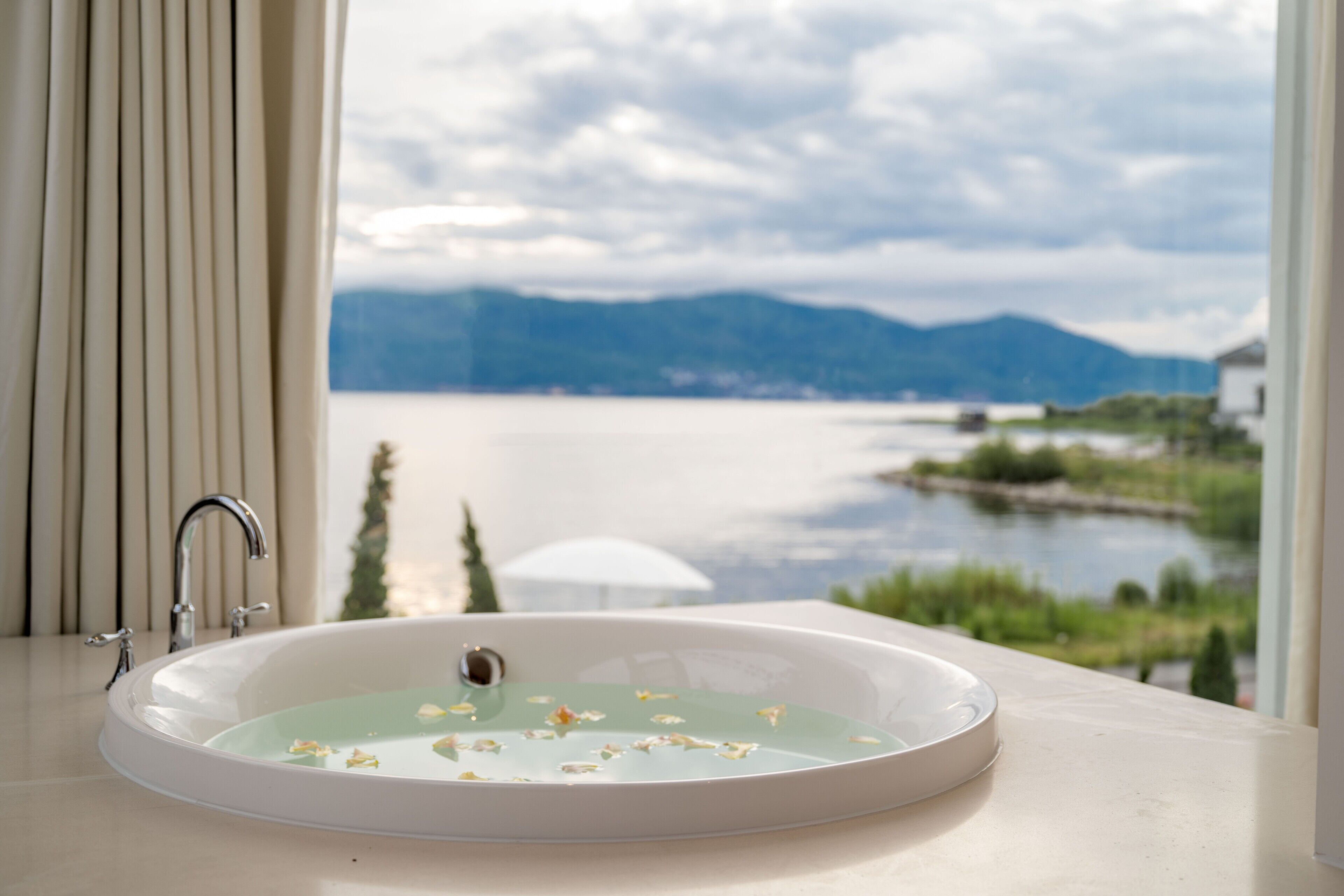 A bathroom with a bathtub, a window with a view of a lake and mountains.