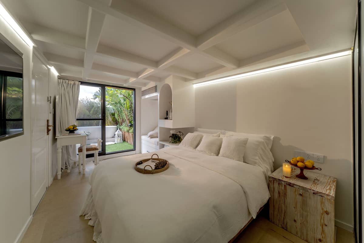 A modern bedroom with a large bed, a small table, and a view of the outdoors.