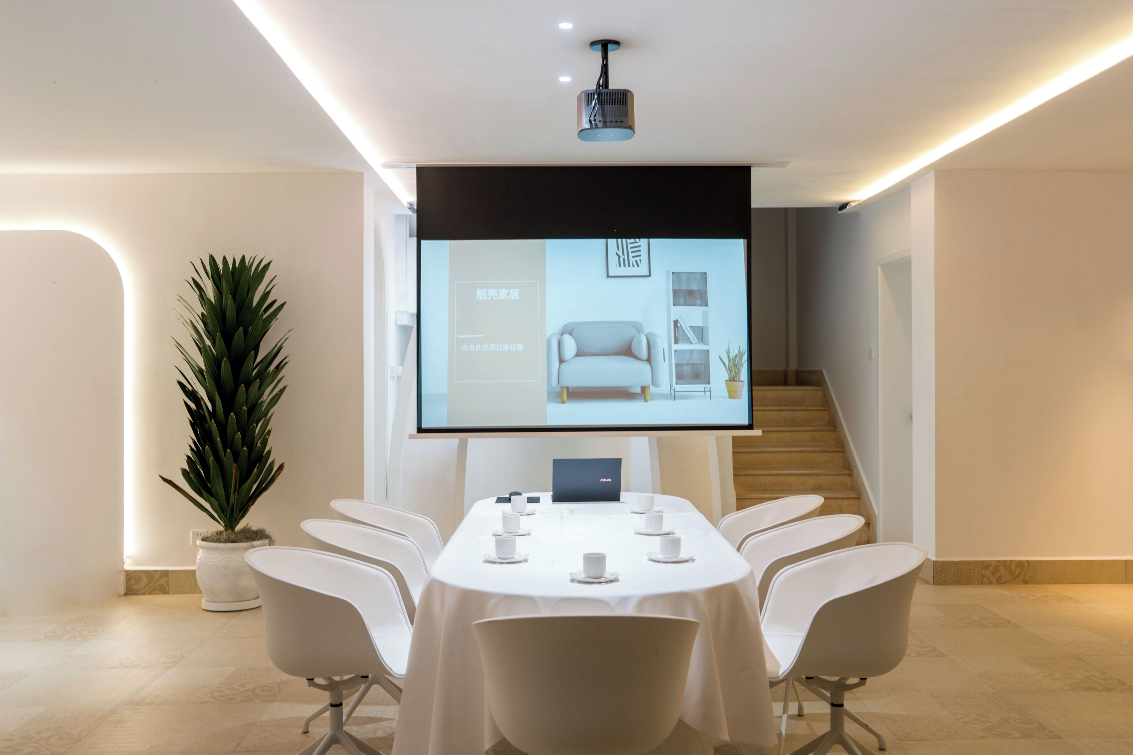 Une salle de conférence moderne équipée d’un grand écran diffusant une présentation, d’un ordinateur portable et d’une table préparée pour une réunion.
