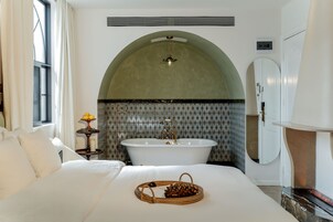 Habitación de hotel con una cama grande, una bañera y un arco decorativo en la pared.