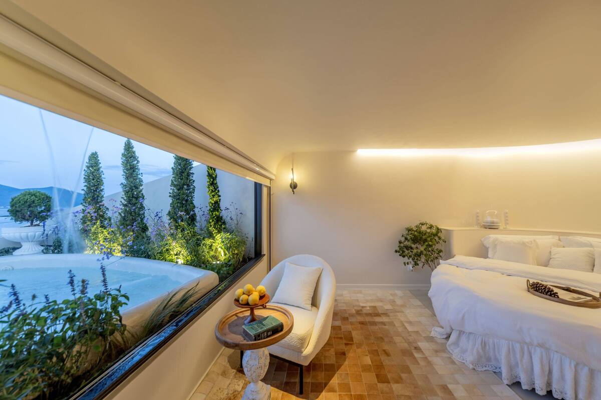 A bedroom with a large window, a sofa, a bedside table, and a bed.