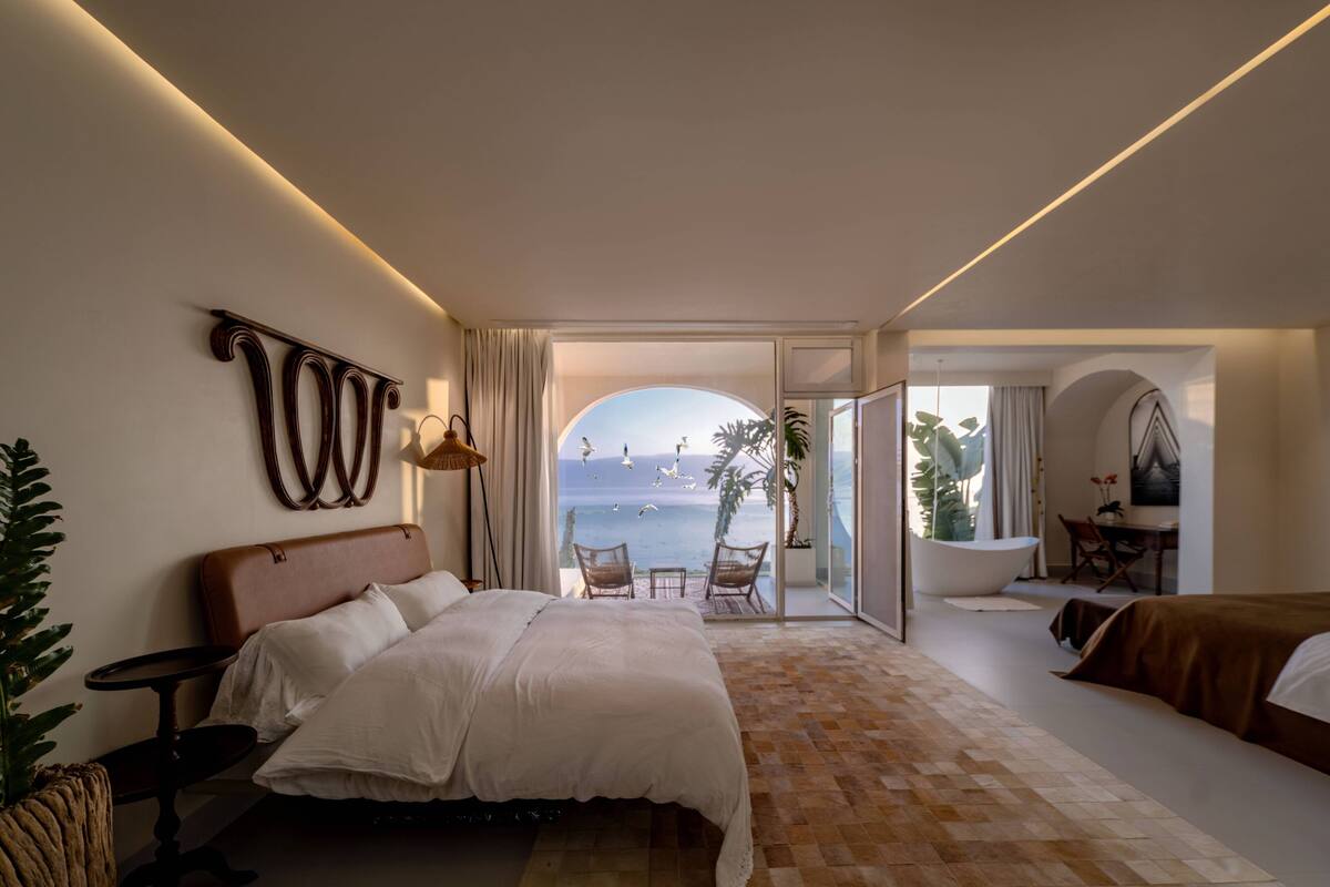 A modern hotel room with a large bed, a seating area with a view of the sea, and a balcony with a view of the ocean.