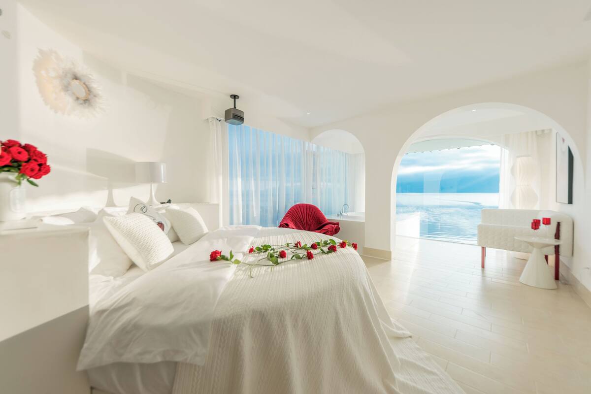 A spacious bedroom with a large bed, a vanity, and a view of the sea.