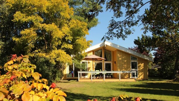 A modern house with a covered patio, surrounded by lush greenery and trees. - Ferienhaus mit Sauna im Ferienpark Mirow (Mirow)