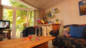 A cozy living room with a wooden table, a sofa with cushions, a television, and a bookshelf. - Ferienhaus mit Sauna im Ferienpark Mirow (Mirow)
