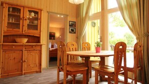 A wooden dining room with a round table and six chairs, a cabinet with glass doors, and a large window with curtains. - Ferienhaus mit Sauna im Ferienpark Mirow (Mirow)