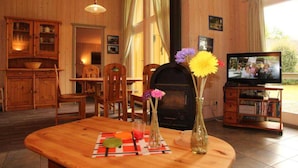 A cozy living room with wooden walls and furniture, a fireplace, a television, and a dining area with a table set for two. - Ferienhaus mit Sauna im Ferienpark Mirow (Mirow)