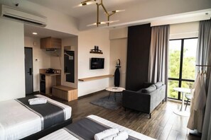 Habitación de hotel con dos camas, un sofá, una mesita, un televisor y una ventana con cortinas.