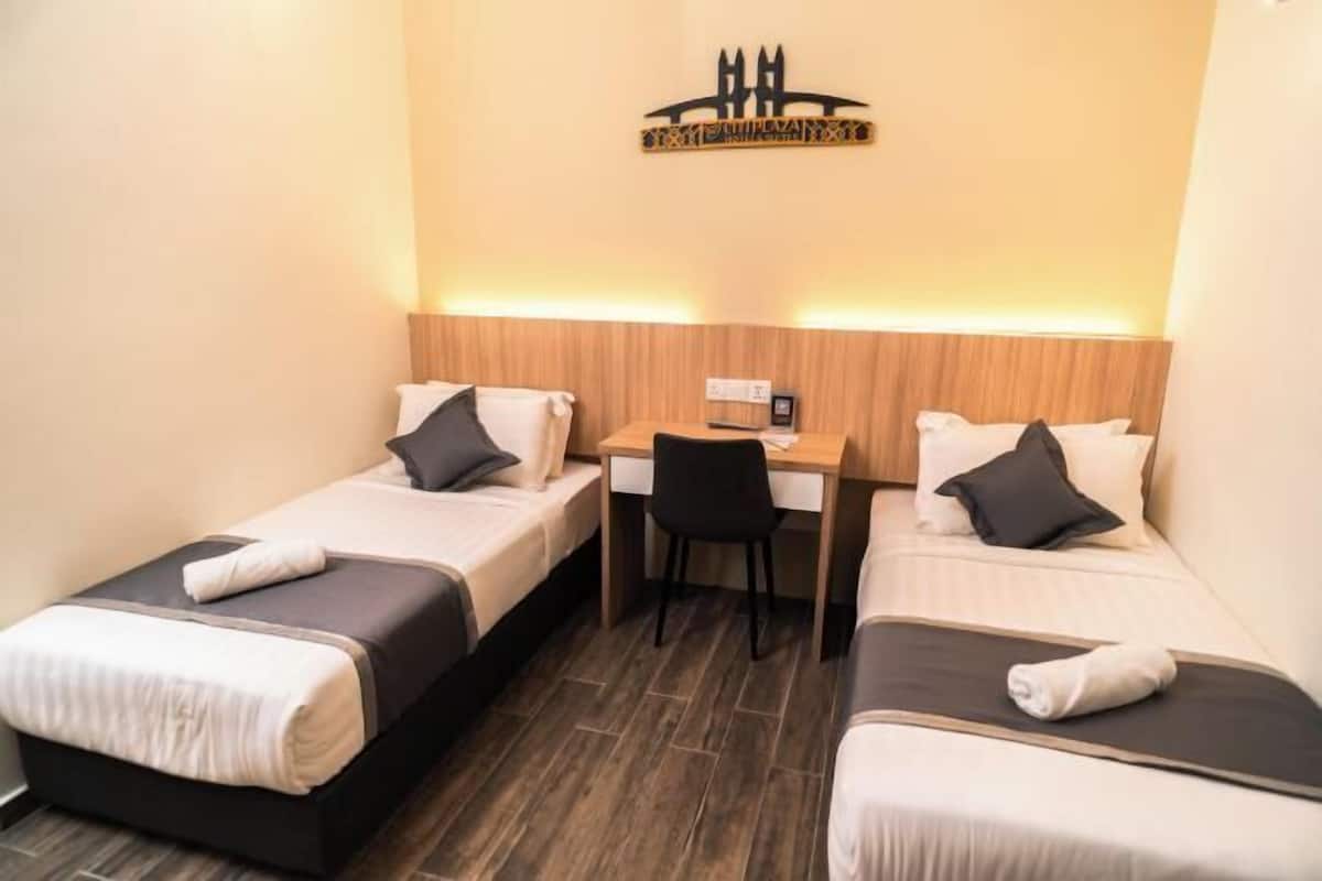 A hotel room with two single beds, a desk, and a chair.