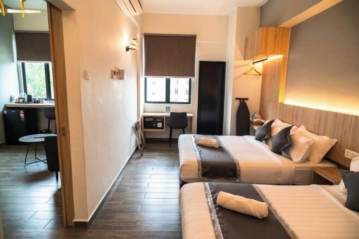 A modern hotel room with a bed, desk, and chair, a window, and a wall-mounted light fixture.