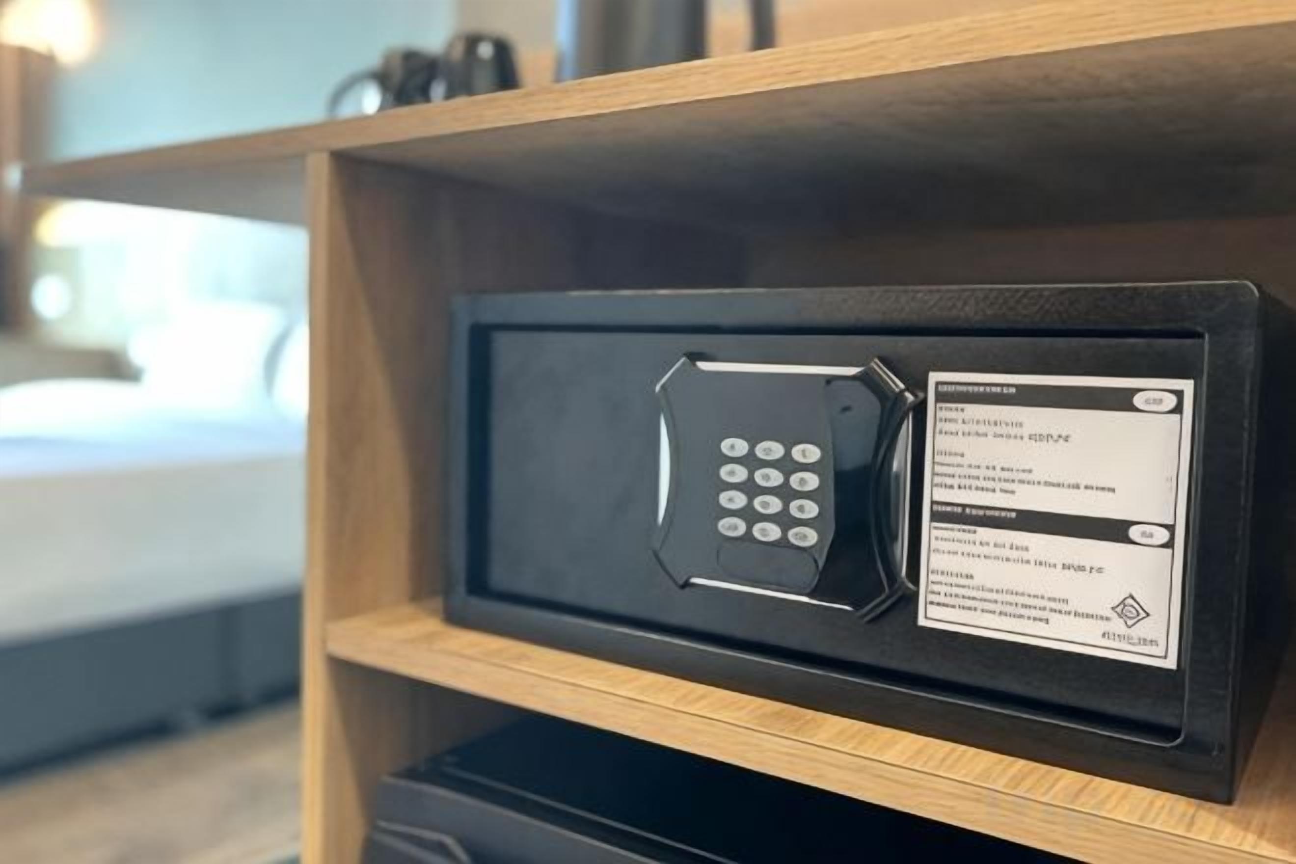 A black safe with a keypad and a label inside a wooden shelf.