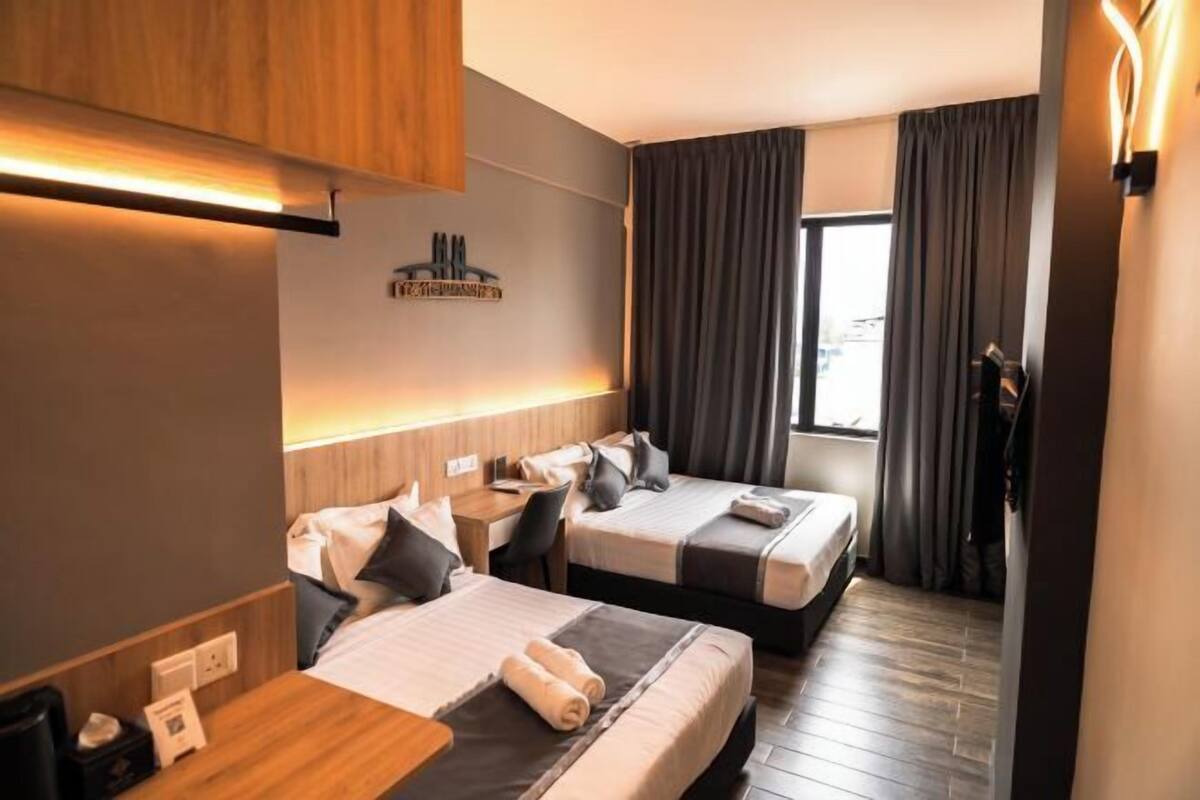 A hotel room with two beds, a desk, and a window with curtains.
