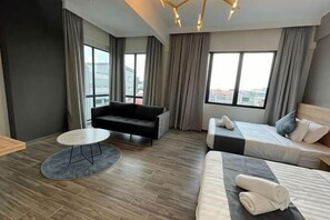 Una habitación de hotel moderna con sofá, cama, una mesita de centro redonda y ventanas amplias.