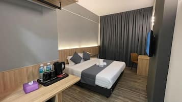 A hotel room with a bed, a desk, a chair, a TV, and a window with curtains.