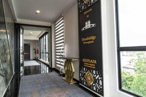 A hotel corridor with a black and gold wall, a reception desk, and a view of the outdoors. - DJ Citi Plaza Hotel & Suites (Kuala Terengganu)