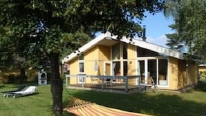 Een geel huis met een veranda, een hangmat en een ligstoel.