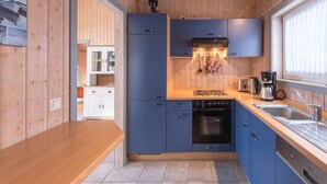 Een kleine keuken met houten wanden, een inbouwoven, een koffiezetapparaat en een raam met gordijnen.