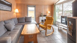 Een gezellige kamer met een houten plafond, een bank, een schommelstoel, een tafel en een televisie.