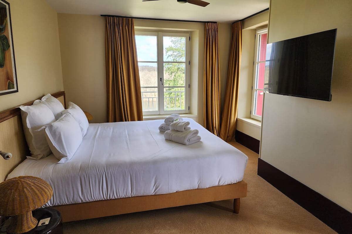 Una habitación de hotel con una cama, una ventana con cortinas, un televisor y un ventilador de techo.
