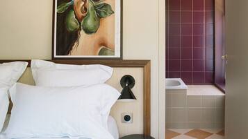 A hotel room with a bed, a nightstand, a wall-mounted lamp, and a framed artwork.