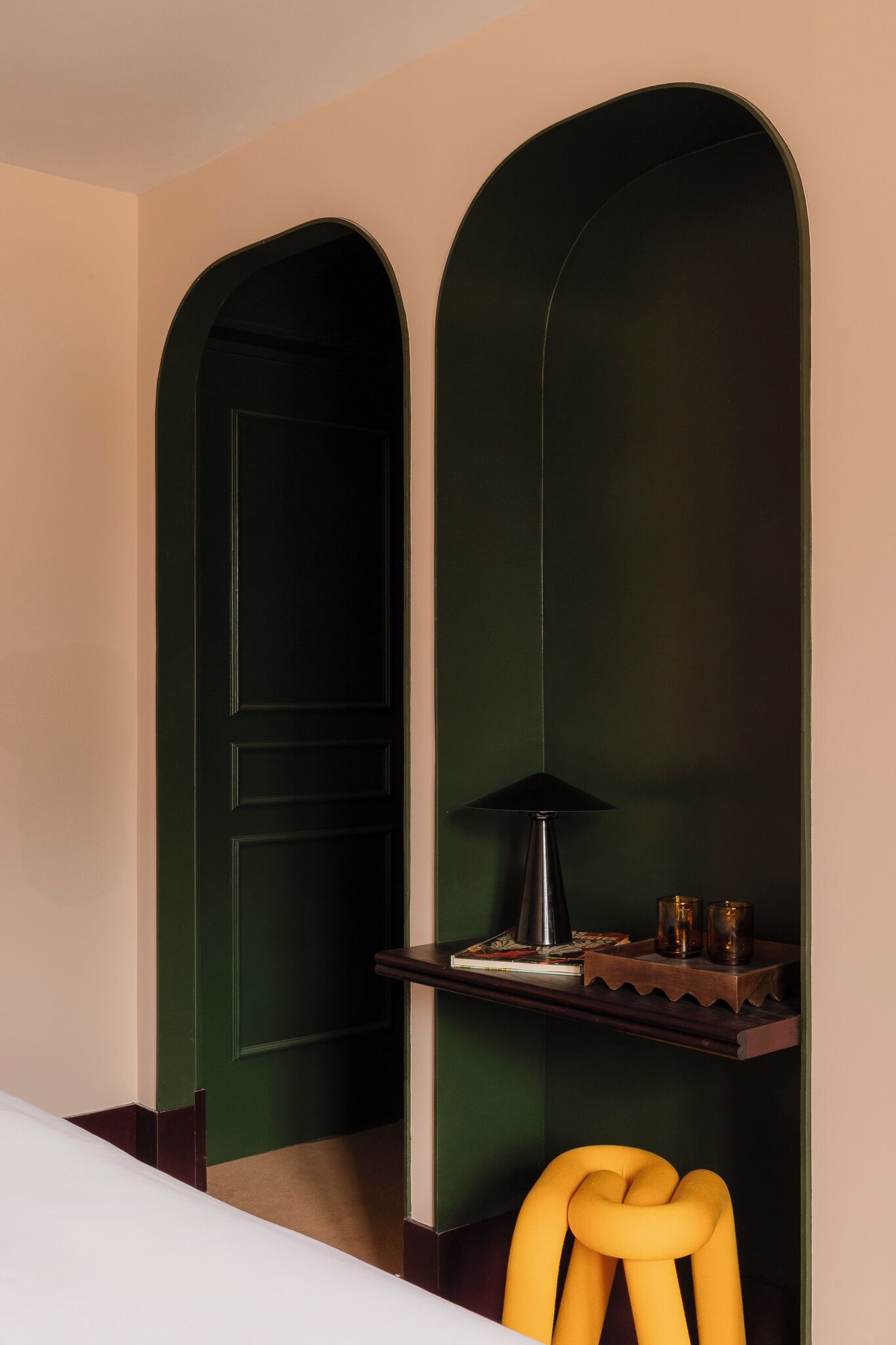 A room with a green door, a desk with a lamp, and a yellow chair.