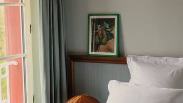 Ein Hotelzimmer mit Bett, einem Fenster mit Vorhängen, einem Wandbild und einer Lampenschirm aus Binsen.