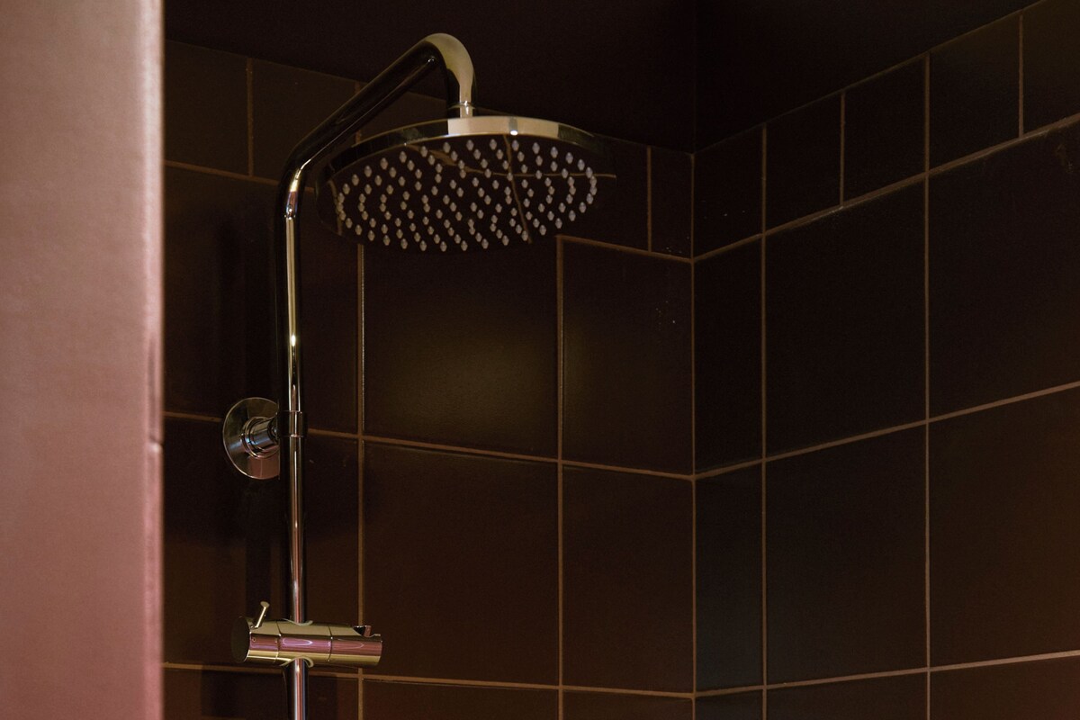 A shower with a handheld head, a wall-mounted control, and a vertical handle.