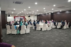 Un salón de conferencias con mesas redondas y sillas blancas, dispuesto en forma de U.