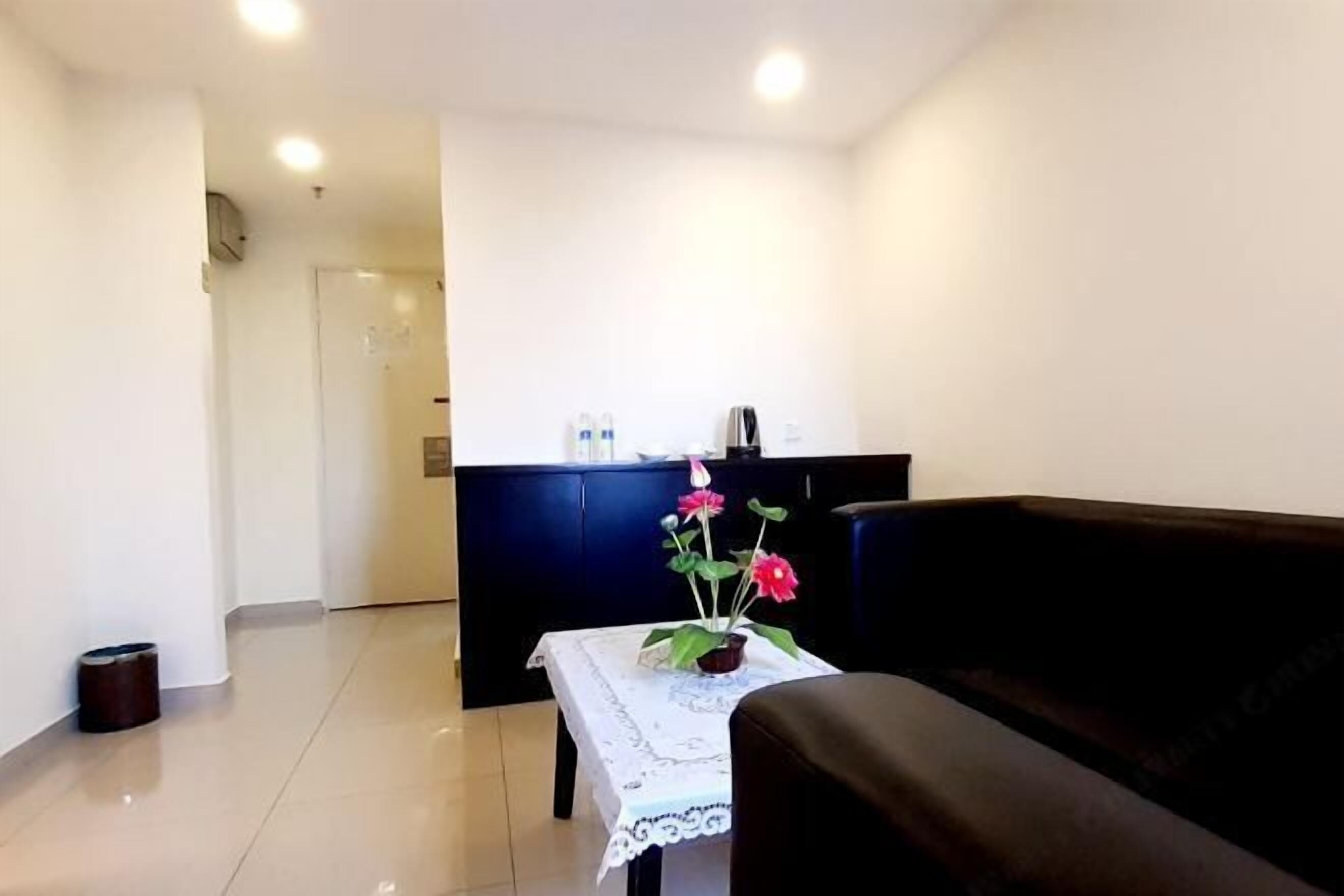 Uma sala de estar com um sofá marrom escuro, uma mesinha com toalha rendada branca e um vaso com flores cor-de-rosa.