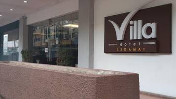 Placa de hotel com o nome 'Villa Hotel Segamat' e uma área de recepção com um banco de pedra.