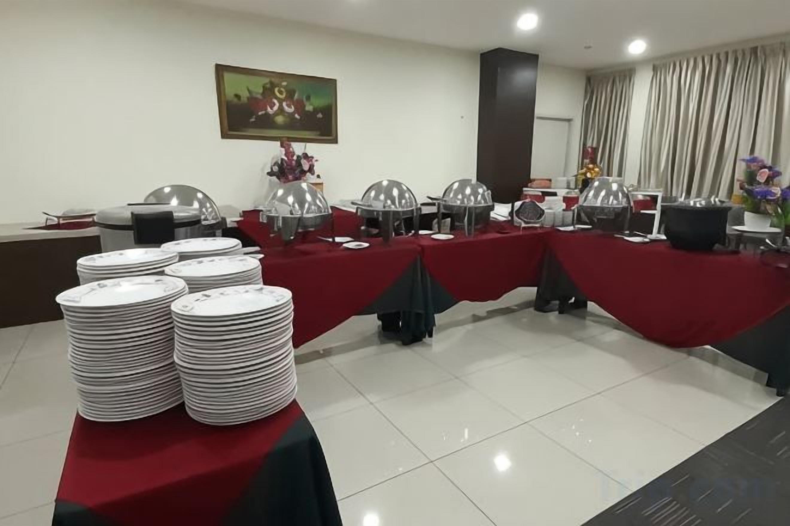 Une salle de conférence avec des tables dressées pour un buffet, chacune recouverte d’une nappe rouge et agrémentée de plats de service en argent.