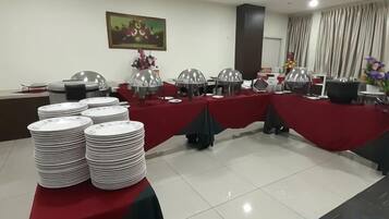 Une salle de conférence avec des tables dressées pour un buffet, chacune recouverte d’une nappe rouge et agrémentée de plats de service en argent.