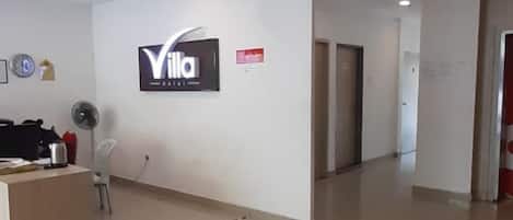 A hotel reception area with a reception desk, a wall-mounted sign, and a hallway leading to other rooms.