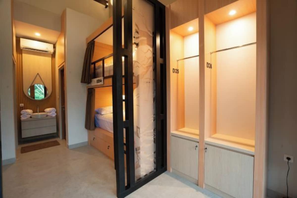 A hotel room with a bunk bed, a small bathroom with a toilet and sink, and a large mirror.