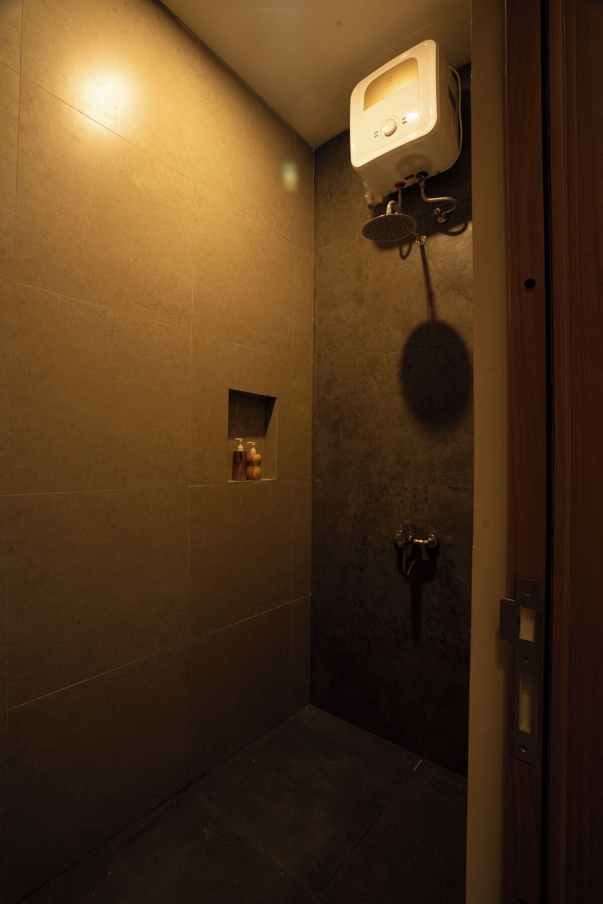 A small, dimly lit shower area with a handheld showerhead and a wall-mounted control panel.