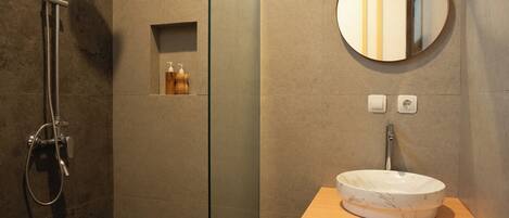 A modern bathroom with a glass shower enclosure, a round mirror, and a wooden vanity with a white sink.